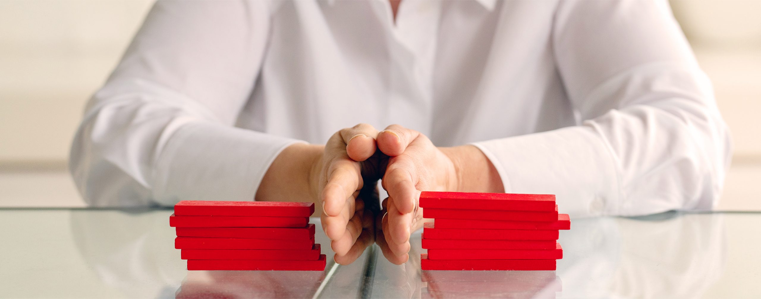 Wirtschaftsmediation Zwei Hände - symbolisch die Mediatorin - trennt zwei Konfliktparteien. Darstegestellt durch zwei rote Bauklotz-Stapel